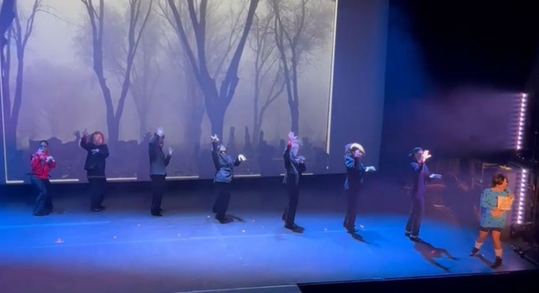 A group of people are dancing on a stage in front of a large screen.