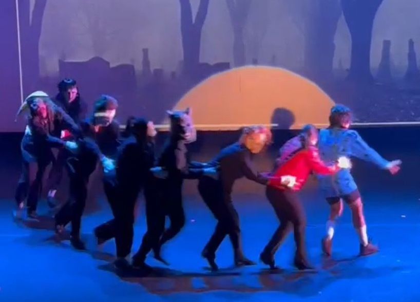 A group of people are dancing on a stage with trees in the background