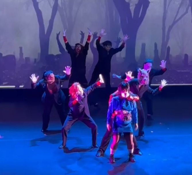 A group of people are dancing on a stage with trees in the background