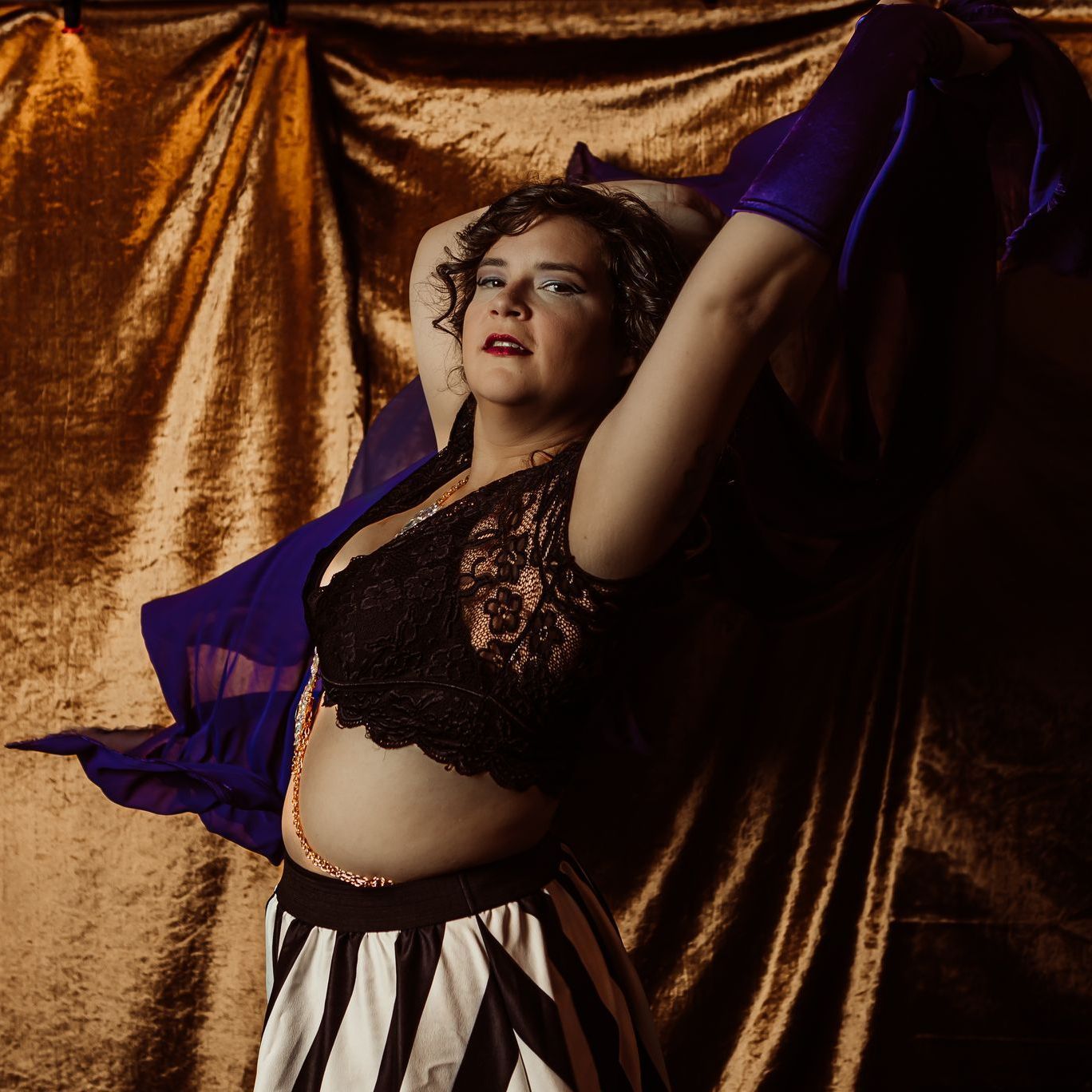 A woman in a black top and striped skirt is standing in front of a gold curtain