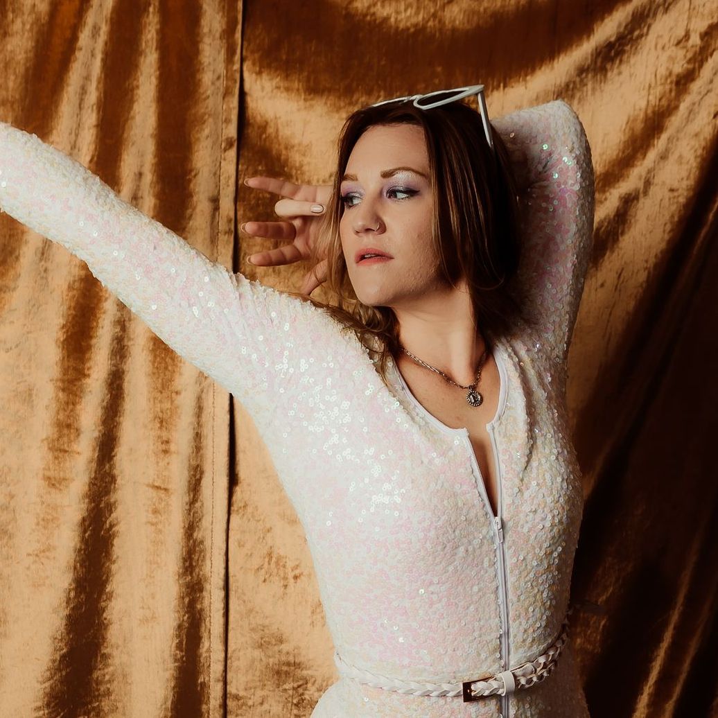 A woman in a white dress is standing in front of a gold curtain.