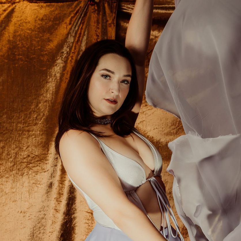 A woman in a white bra is standing in front of a gold curtain