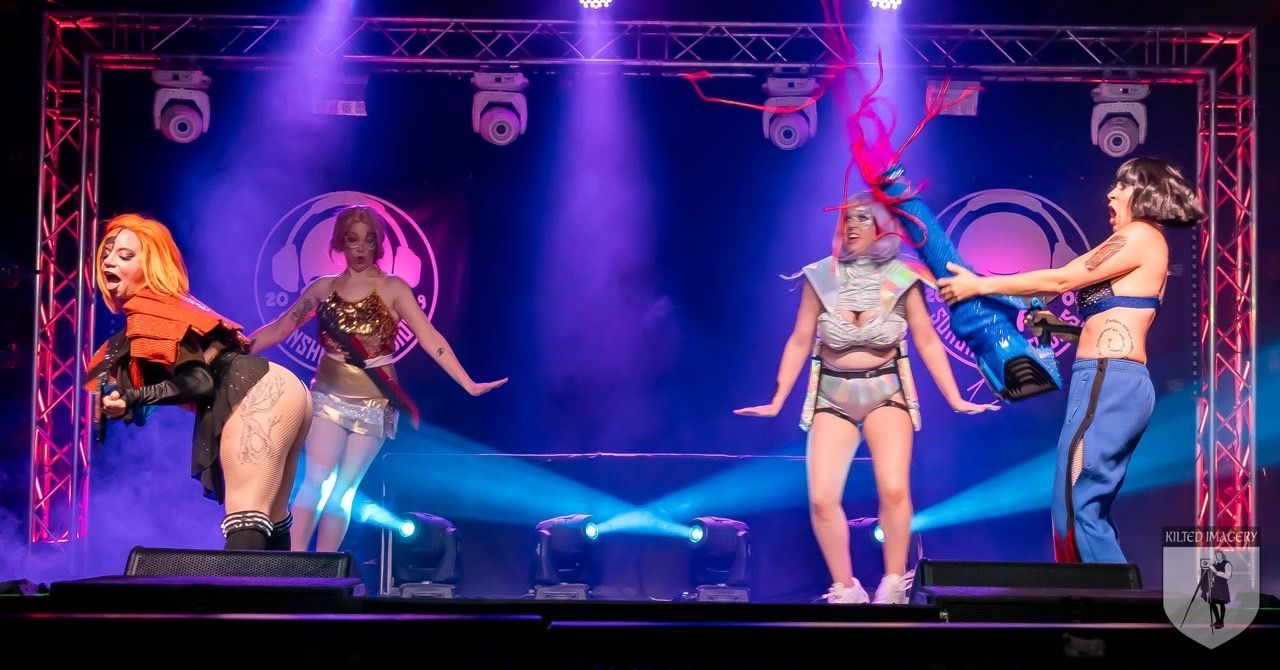 A group of women are dancing on a stage with purple lights.