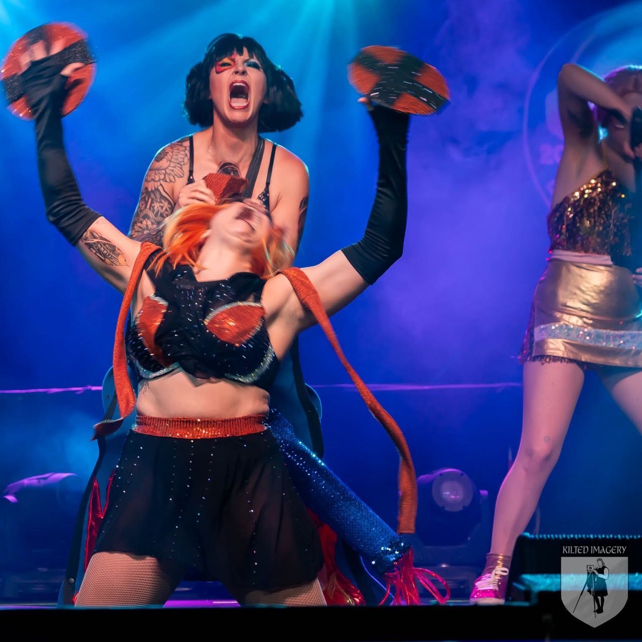 A group of women are performing on a stage with a logo that says but music