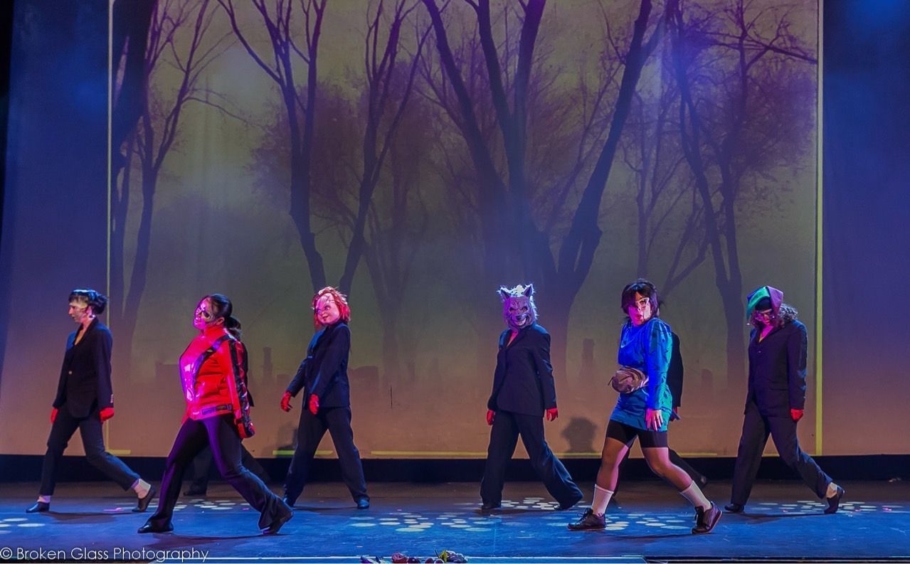 A group of people are walking on a stage with trees in the background.