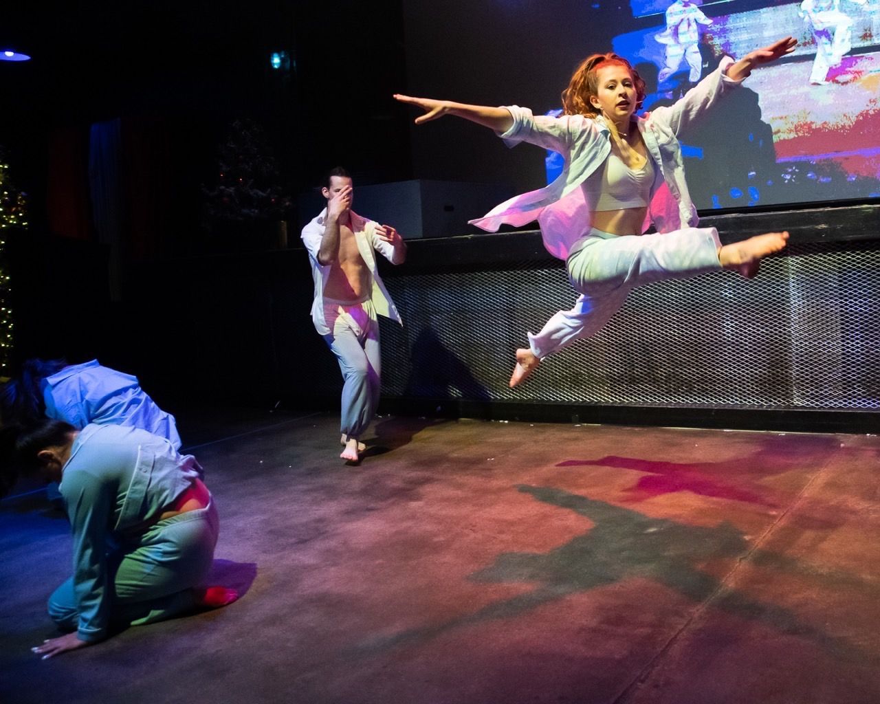 A group of people are dancing on a stage and one of them is jumping in the air.