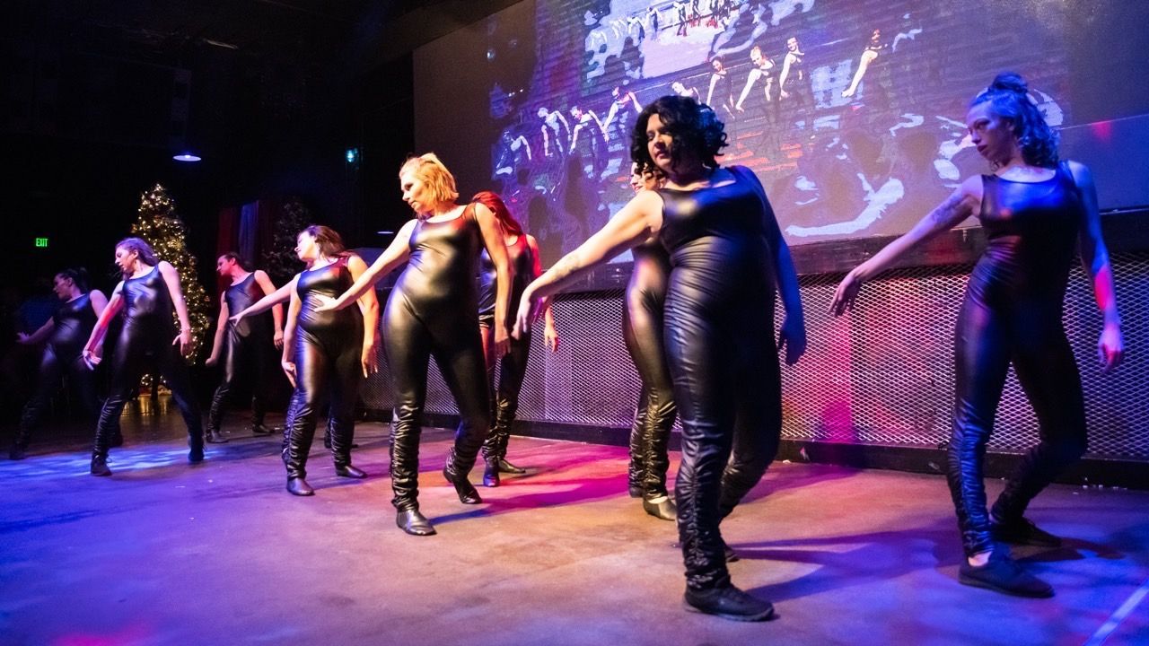 A group of women are dancing on a stage in front of a large screen.