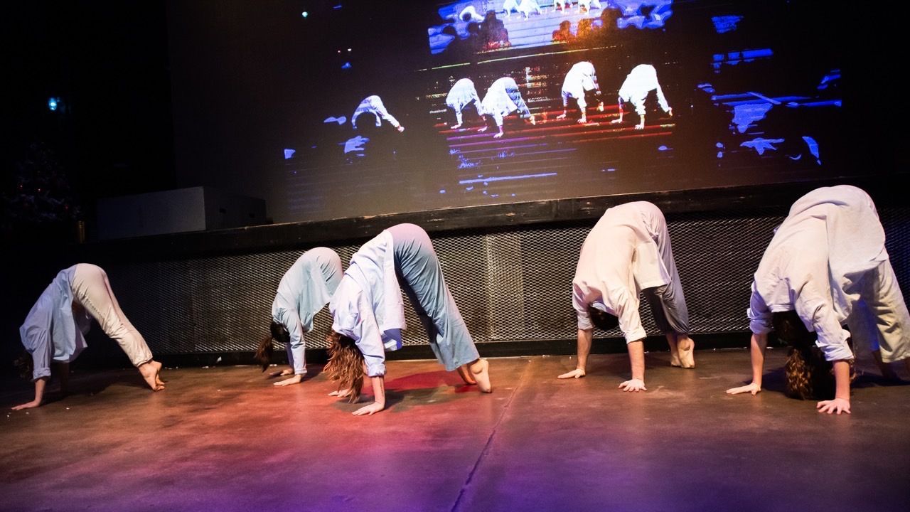 A group of people are doing handstands on a stage in front of a large screen.