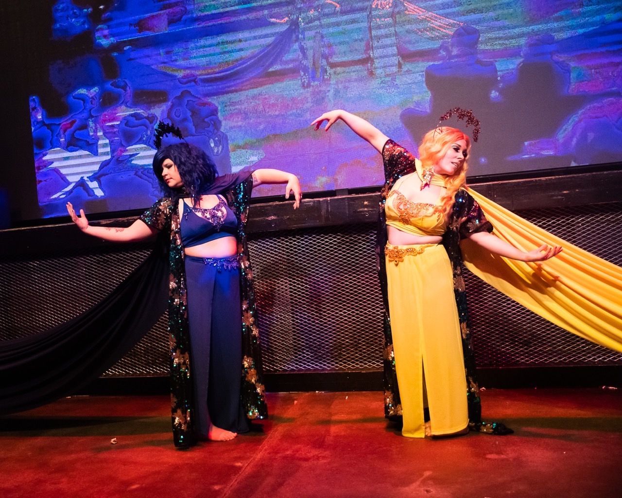 Three women are dancing on a stage in front of a large screen.
