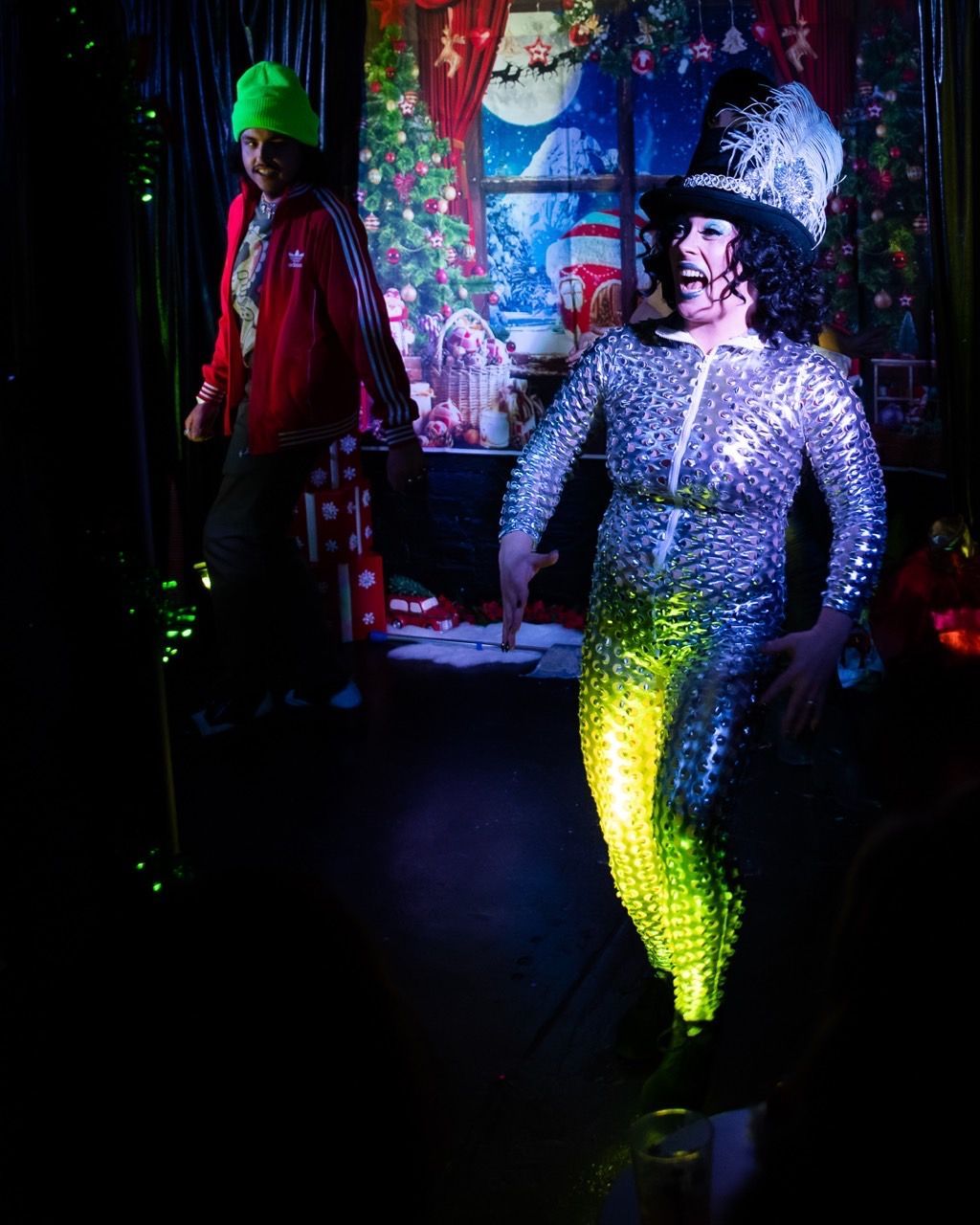 A man in a mermaid costume is dancing in front of a christmas tree