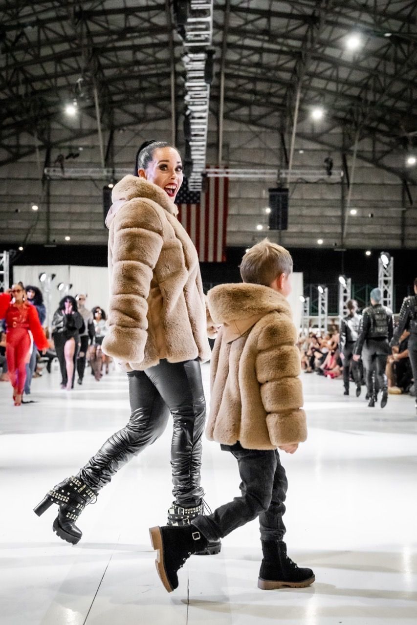 A woman and a child are walking down a runway at a fashion show.