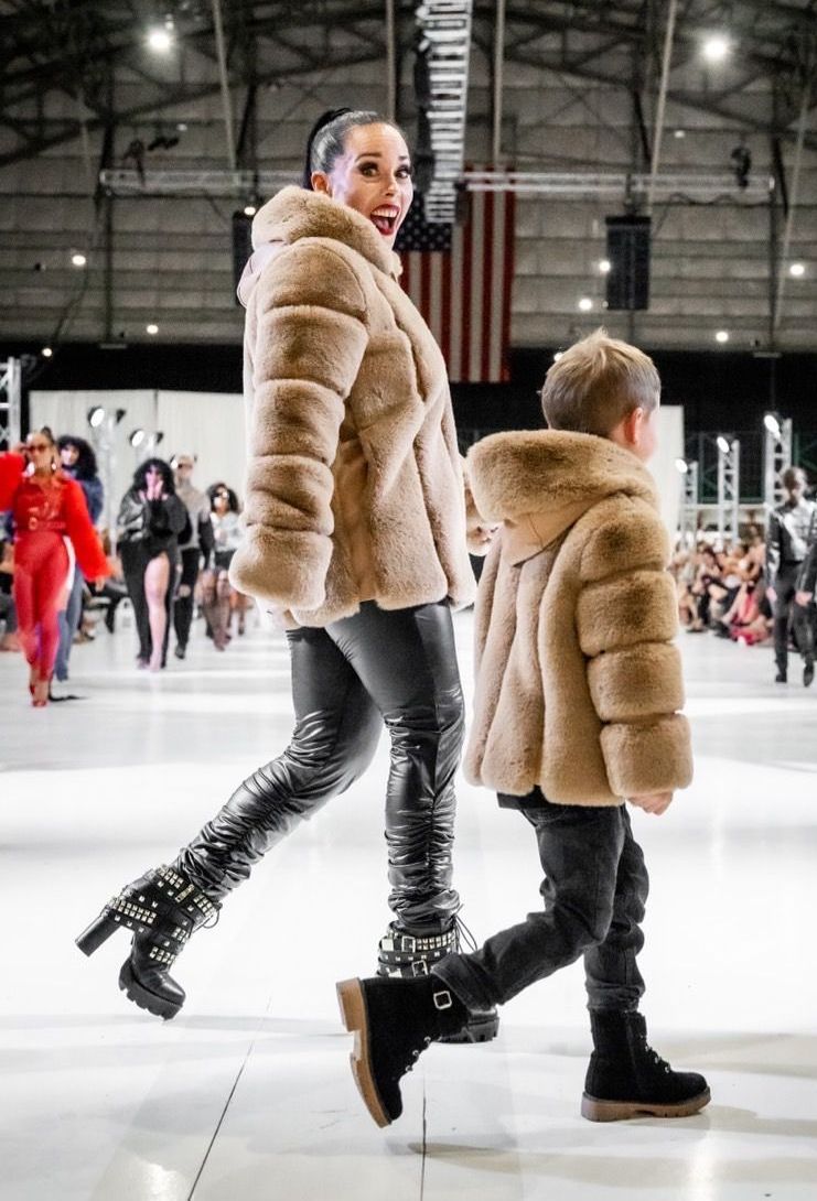 Woman and child in matching tan fur coats and black boots walking on a runway.