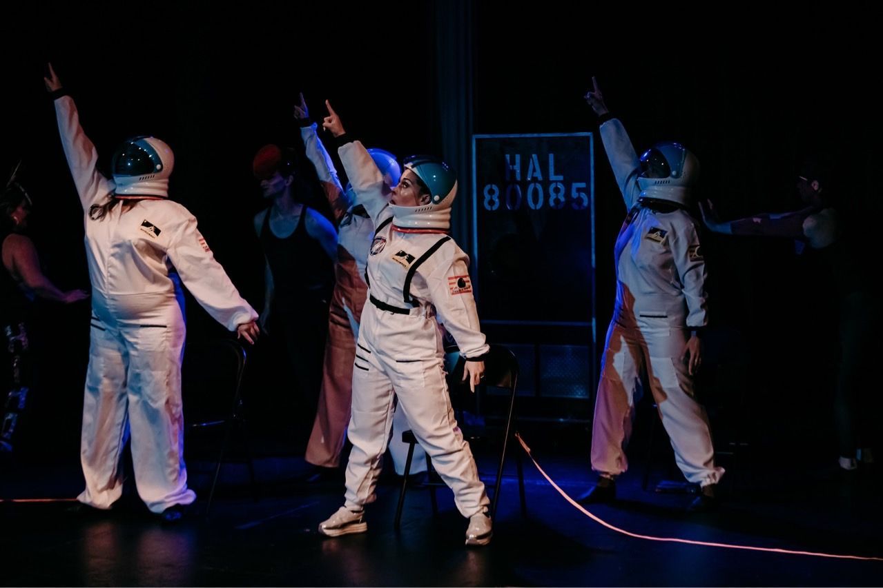 A group of people in space suits are dancing on a stage.