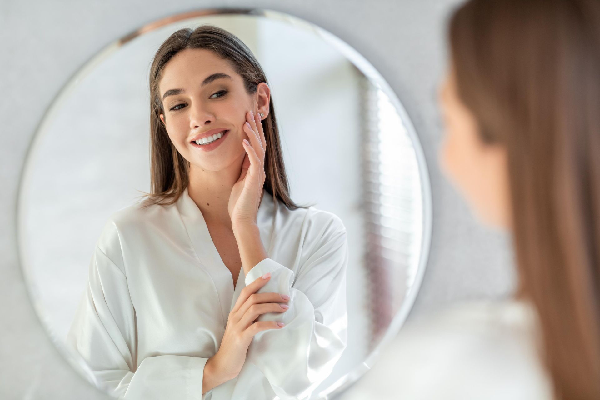 A woman is looking at her face in a mirror.