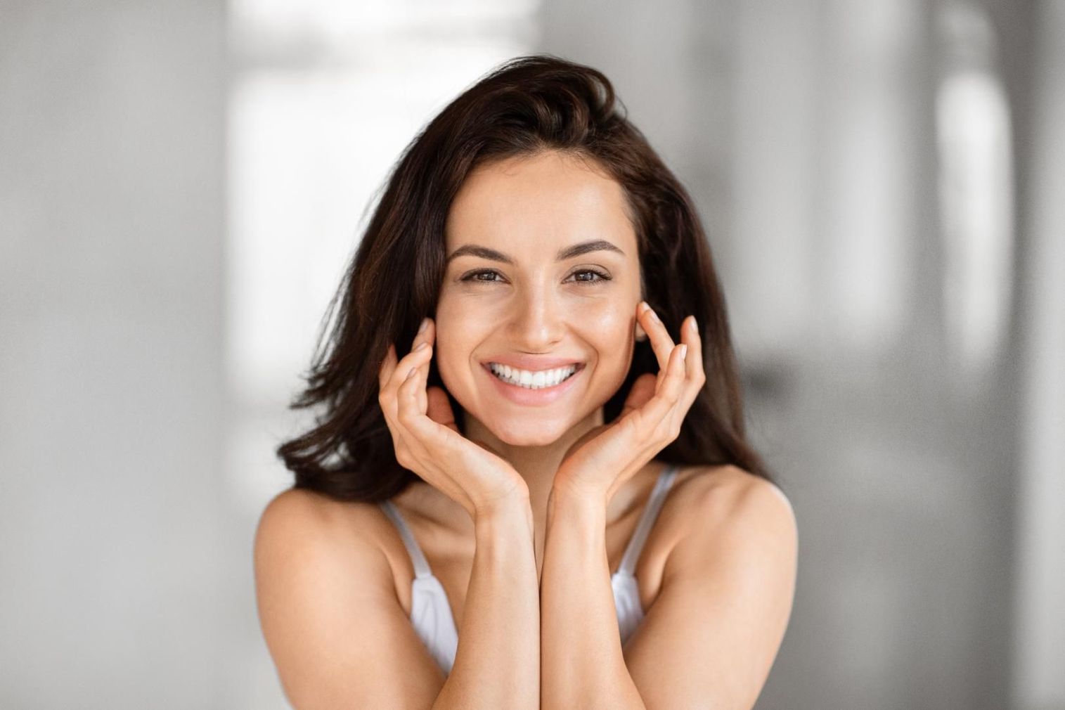 A woman is smiling with her hands on her face.