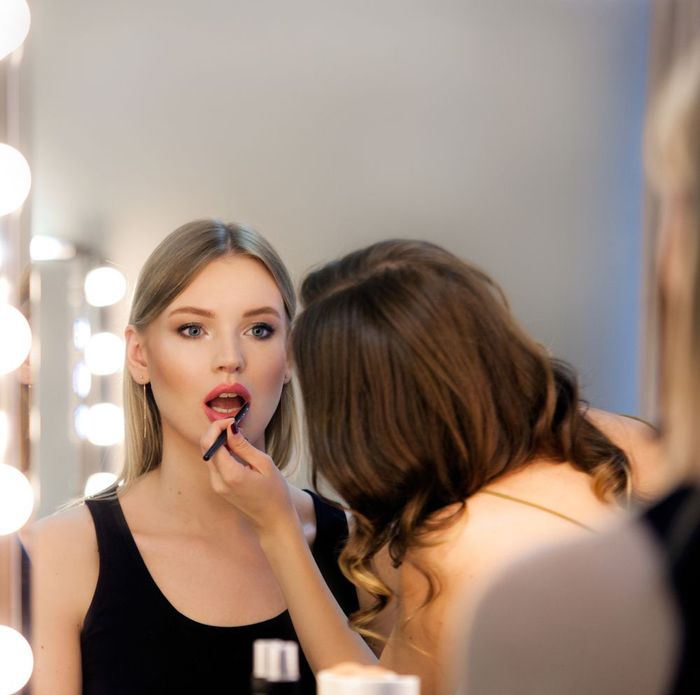 A woman is applying lipstick to another woman in front of a mirror