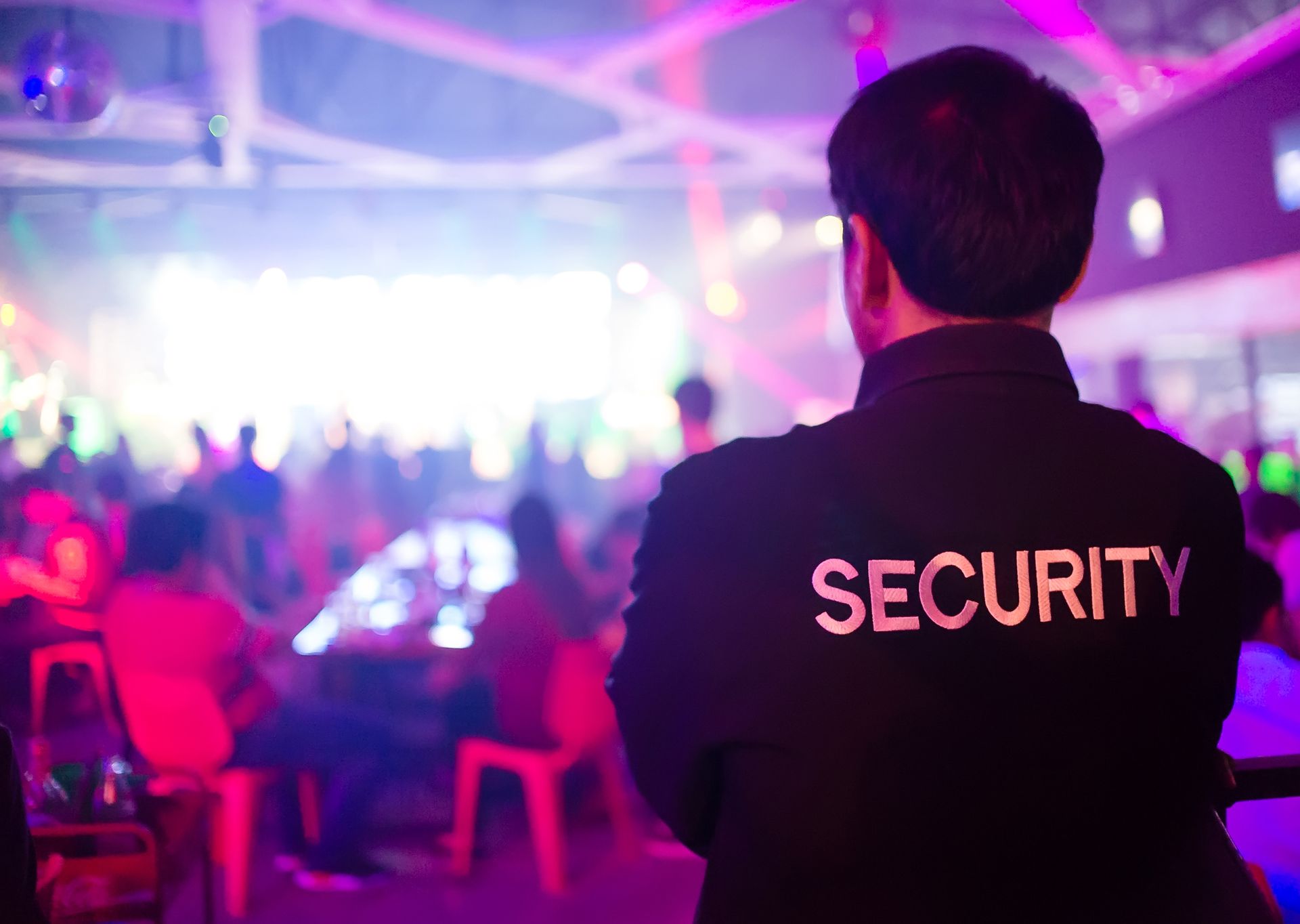 Security guard observing a crowded, brightly lit nightclub.