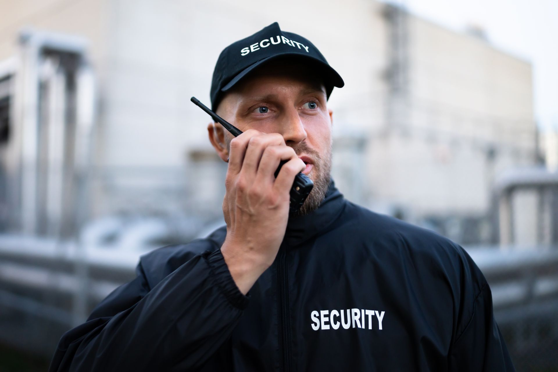 Security guard in black uniform and cap, using a walkie-talkie.