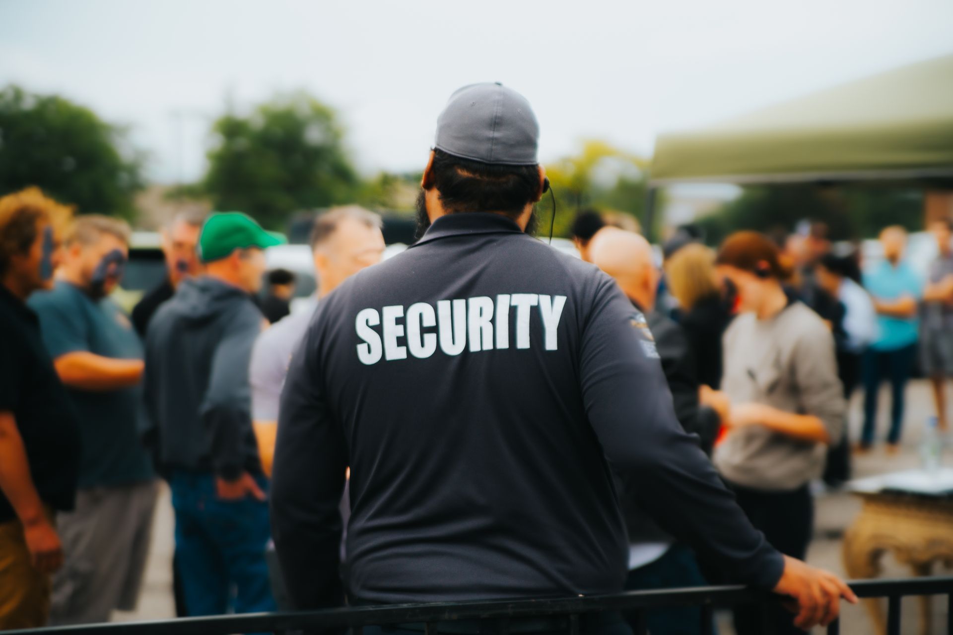 Security guard in gray shirt, standing in front of a crowd of people.