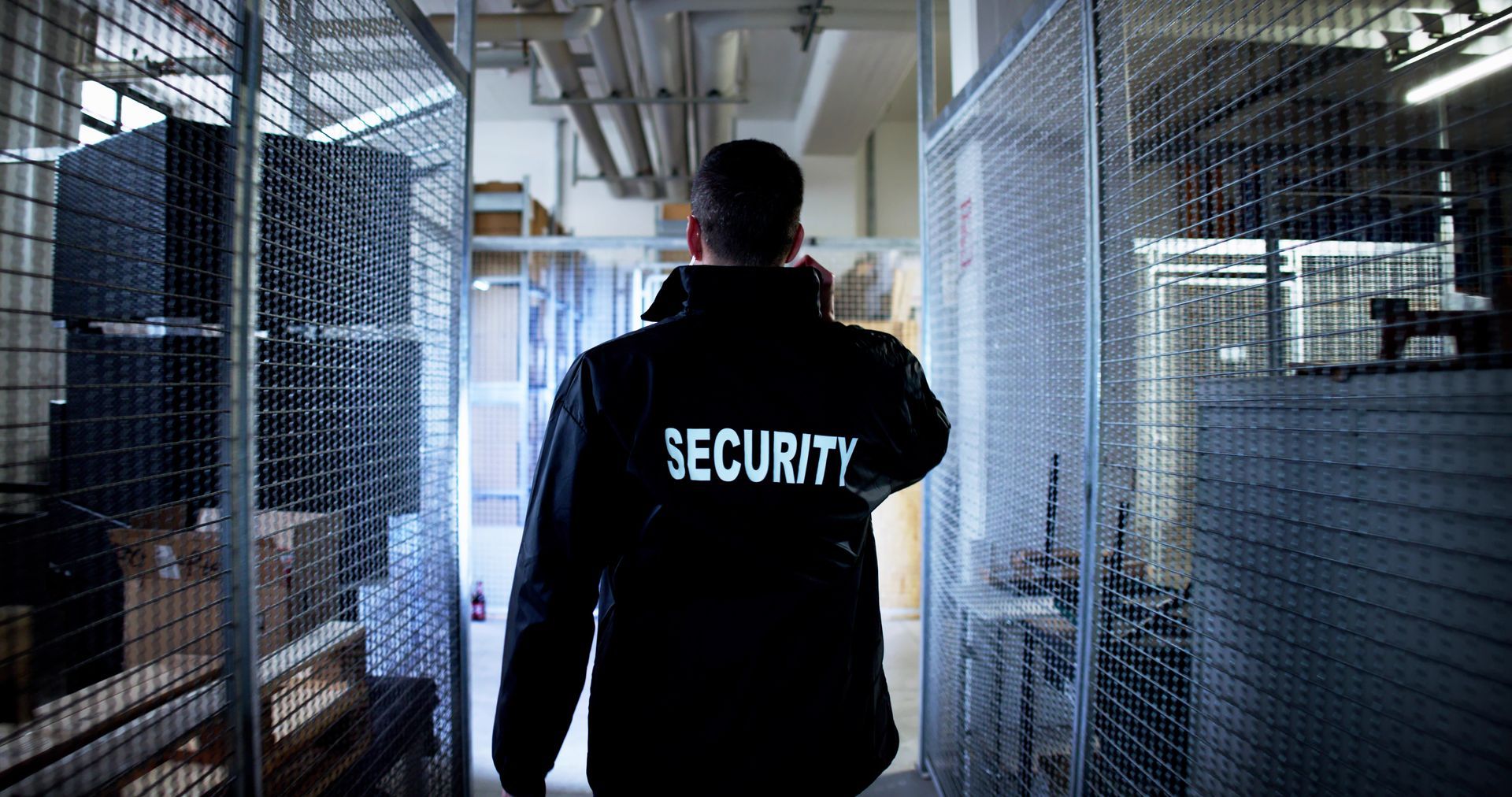 Security guard walking down a storage aisle with metal cages, inspecting the area.