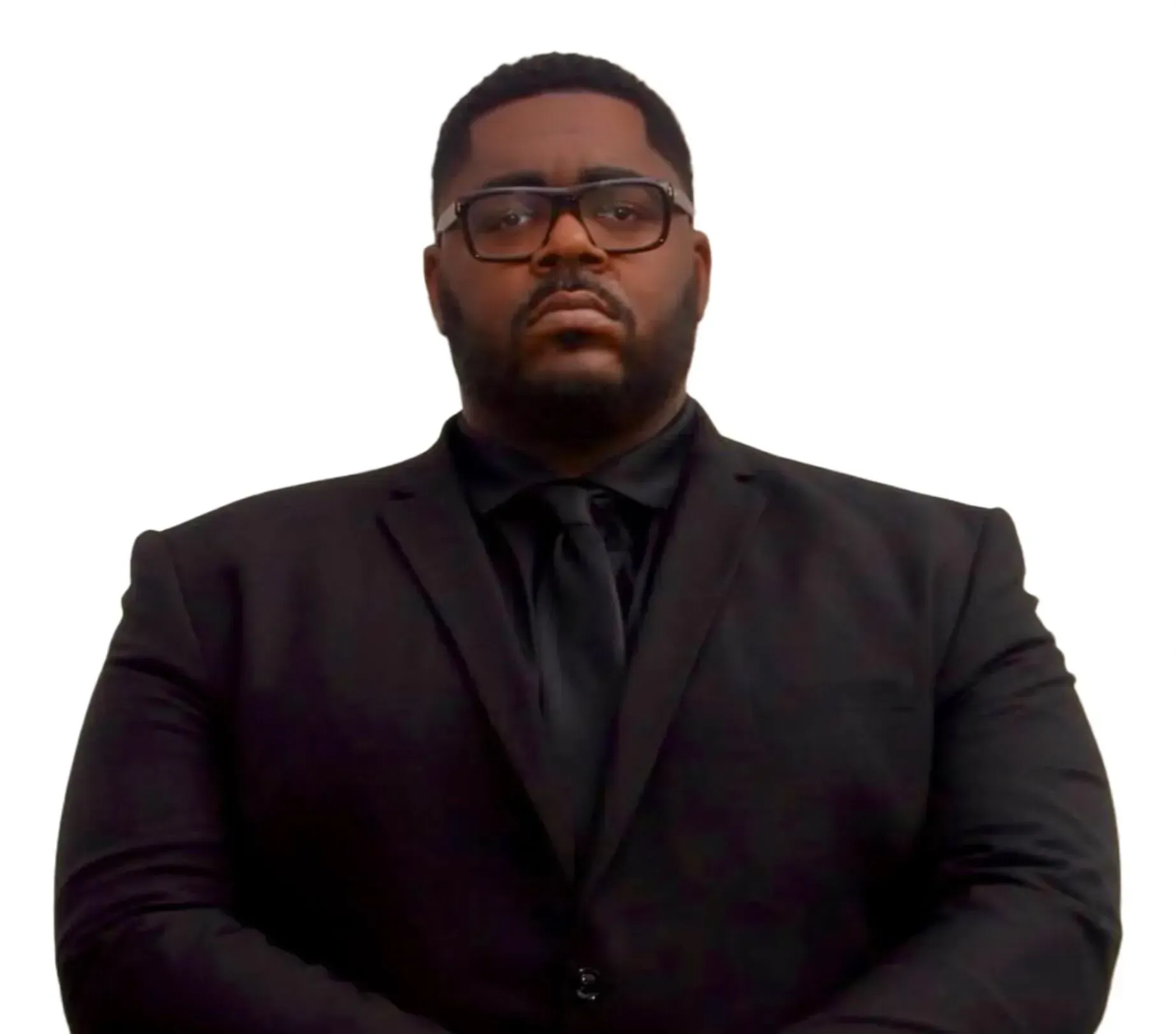 Man wearing glasses and a black suit, staring forward.