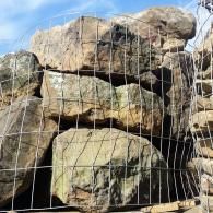 Large stacked boulders behind a wire fence under a bright blue sky