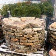 Stacked stone retaining wall blocks on a pallet outdoors, with shrubs in the background