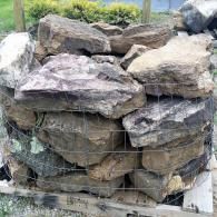 Stacked large gray rocks in a wire mesh basket outdoors