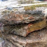 Close-up of layered, weathered rock behind wire mesh netting.