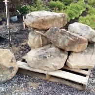 Large boulders stacked on a wooden pallet outdoors in a rocky garden area