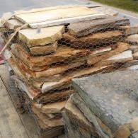 Stacked stone slabs on a pallet outdoors, with one gray slab in the foreground