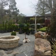 Rock garden with stone fire pit, gravel path, potted plants, and a white pergola in a landscaped yard