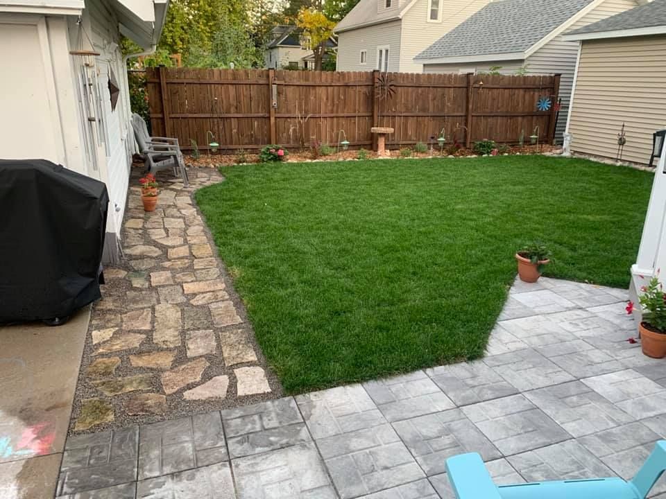 A house on a hillside with stone retaining walls, gravel path, and green grass.