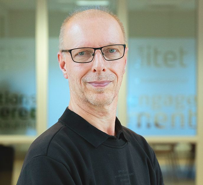 En mand iført briller og en sort skjorte smiler til kameraet