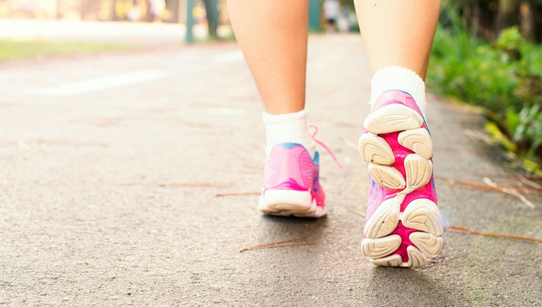 En kvinde går ned ad et fortov iført lyserøde sneakers.