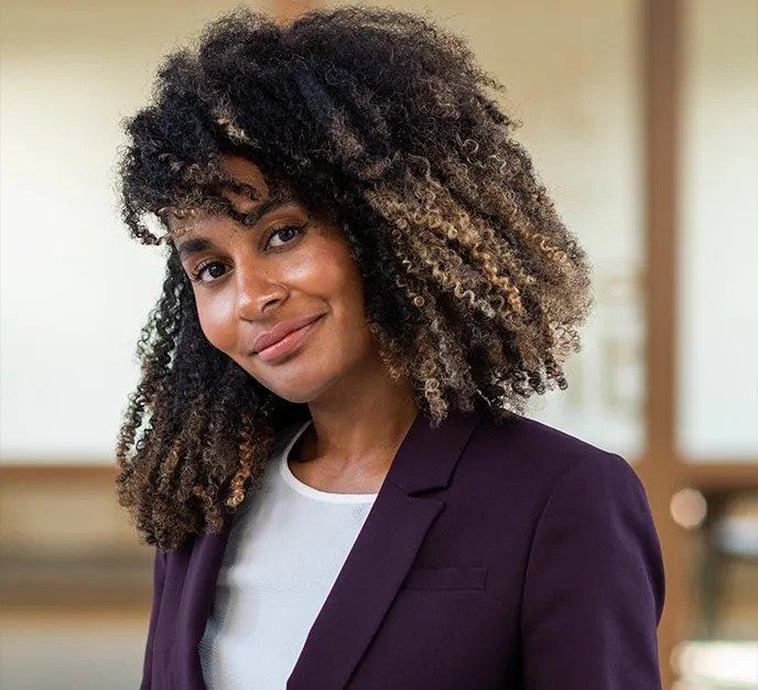 En kvinde med krøllet hår er iført en lilla jakke og smiler.