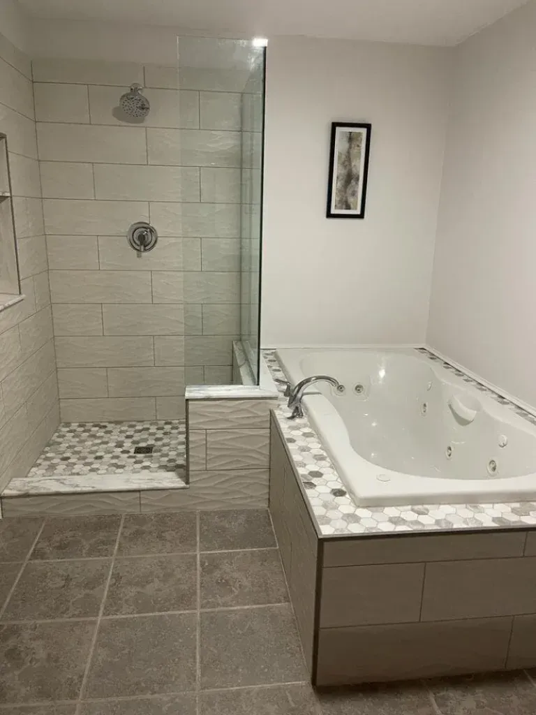 Bathroom with a shower and jacuzzi tub. Gray tiles, white walls, glass shower door.