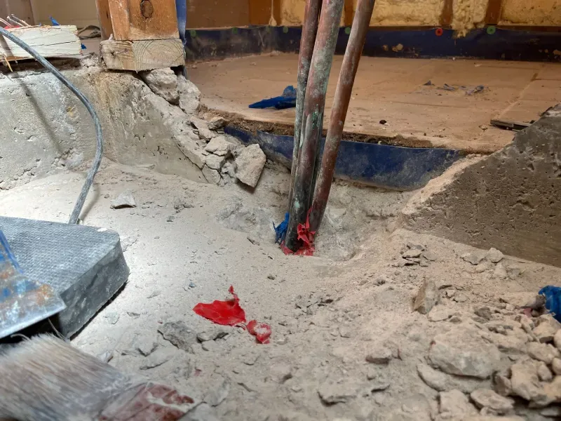 Excavated area with exposed copper pipes, rubble, and concrete; interior.