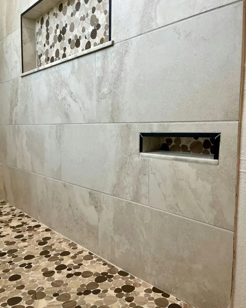 Shower wall with built-in niches. Light-colored tiles with patterned accent tile in the niches. Pebble tile shower floor.