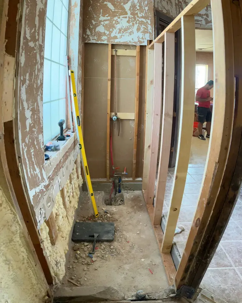 Construction of interior wall and window frame with tools. Person in background.