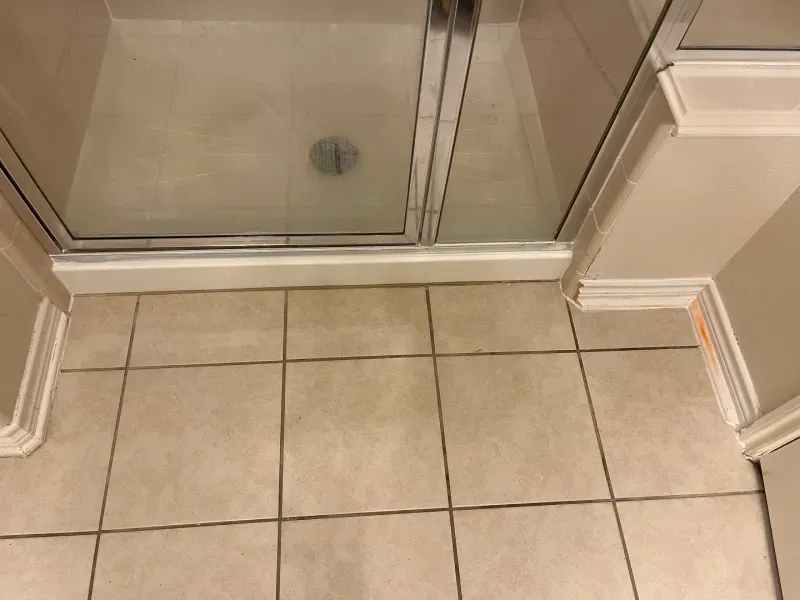 Shower stall with a glass door, tile floor, and beige walls.