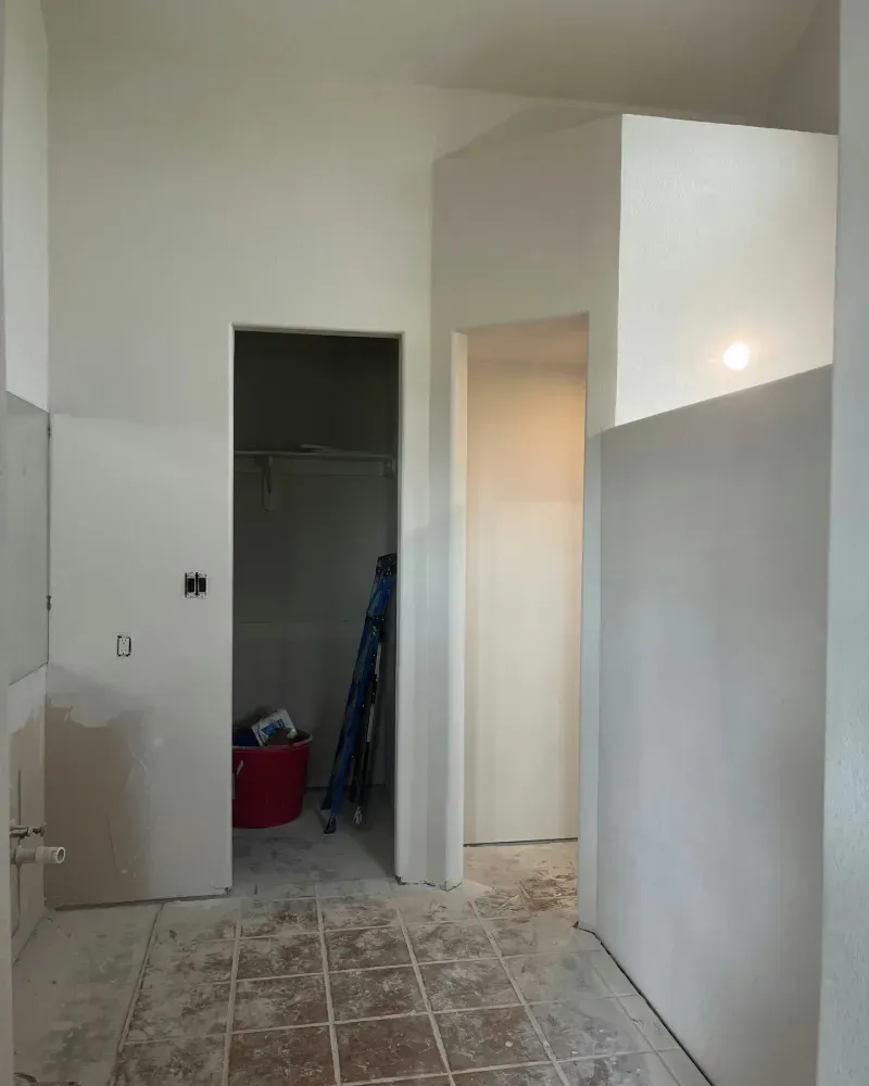 Interior hallway with drywall, unfinished flooring, and doorways leading to other rooms.