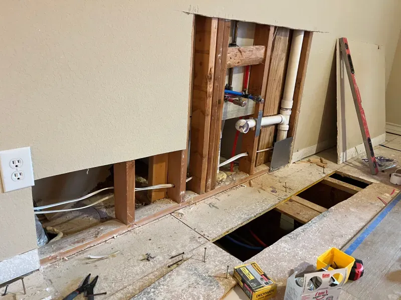 Construction site with exposed plumbing and wall studs. Floorboard removed, electrical wiring visible.