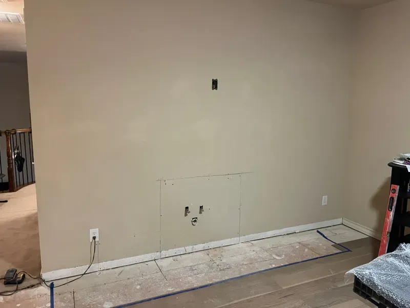 Tan wall with cut-out for a fireplace. Electrical outlets visible. Flooring is partially installed.
