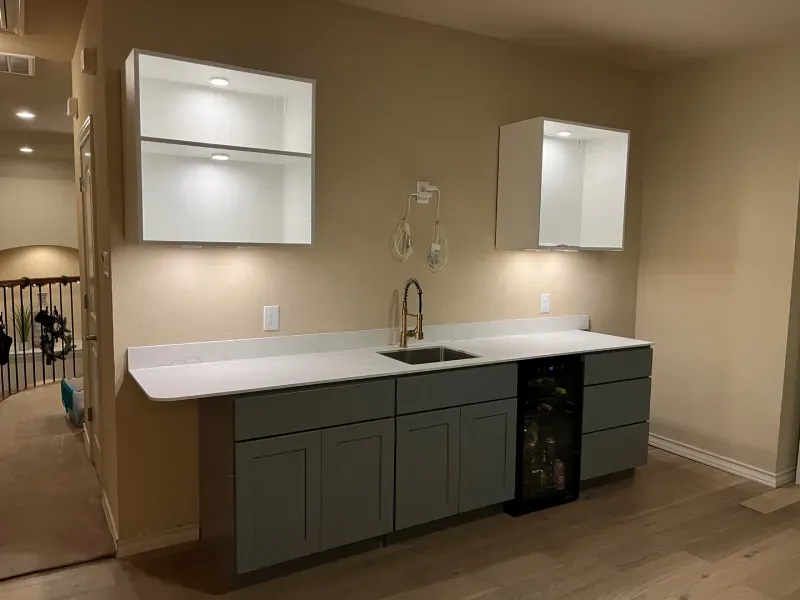 Bar area with white upper cabinets, gray lower cabinets, sink, and wine cooler.