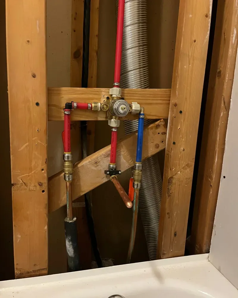 Plumbing pipes of copper and red PEX, with valve and fittings, installed in a wall.