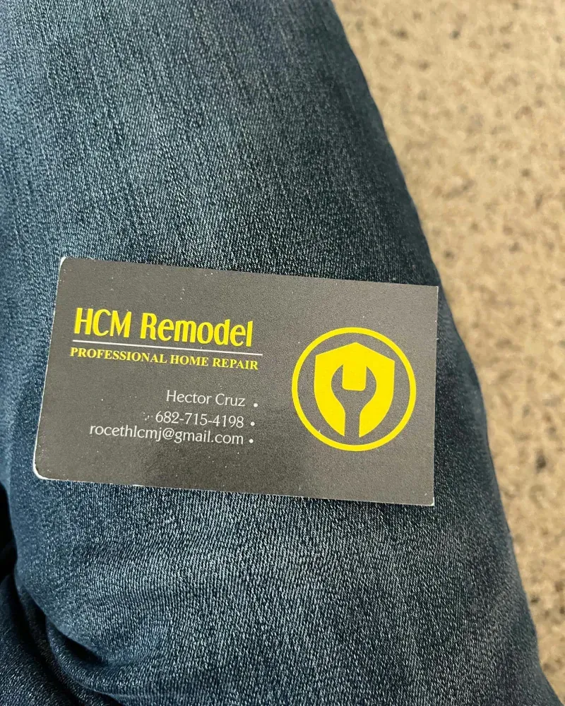 Business card for HCM Remodel, Professional Home Repair, on a person's lap; black card with yellow logo and text.