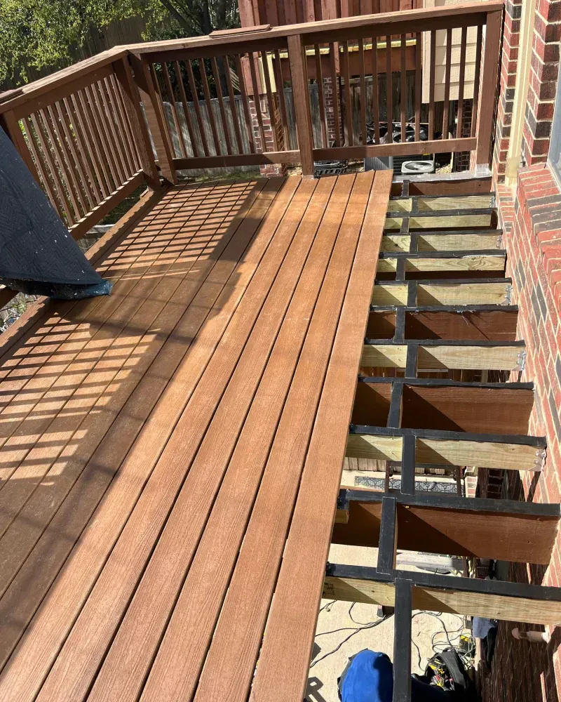 Deck under construction, with wood planks laid on top of the supporting structure next to brick wall.