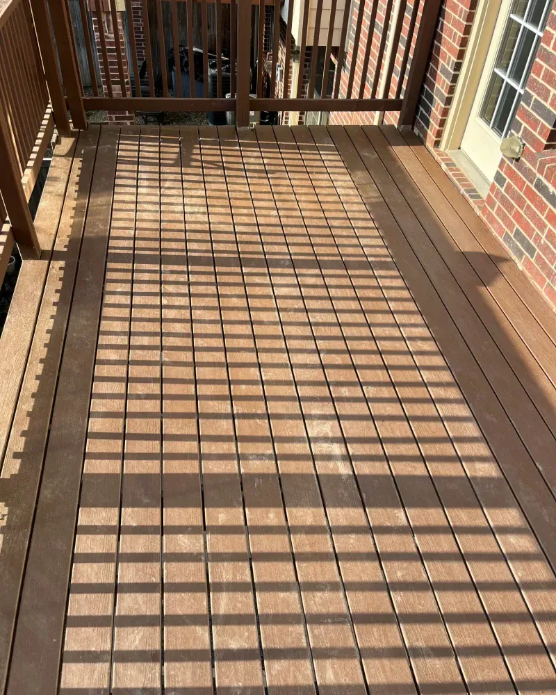 Brown wooden deck with a brick wall and a door.