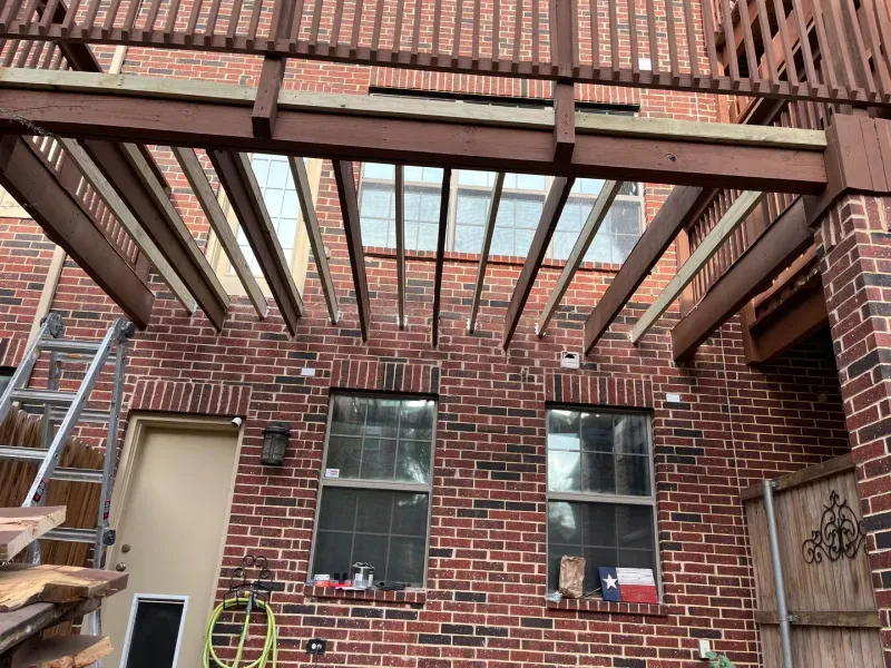Brick house with a wooden pergola, under construction, over windows and a doorway.